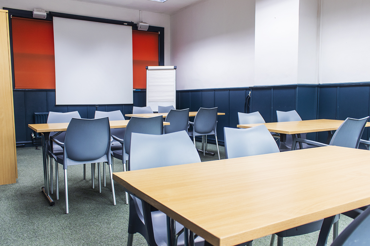 Irving Room in classroom set up with desks, chairs, flipchart and projector screen